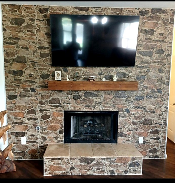Completed fireplace feature-wall rebuild by Affordable Handyman Services with a new mantel, hearth, surround, metal edge trim, grout, caulk, and finish touch-ups.